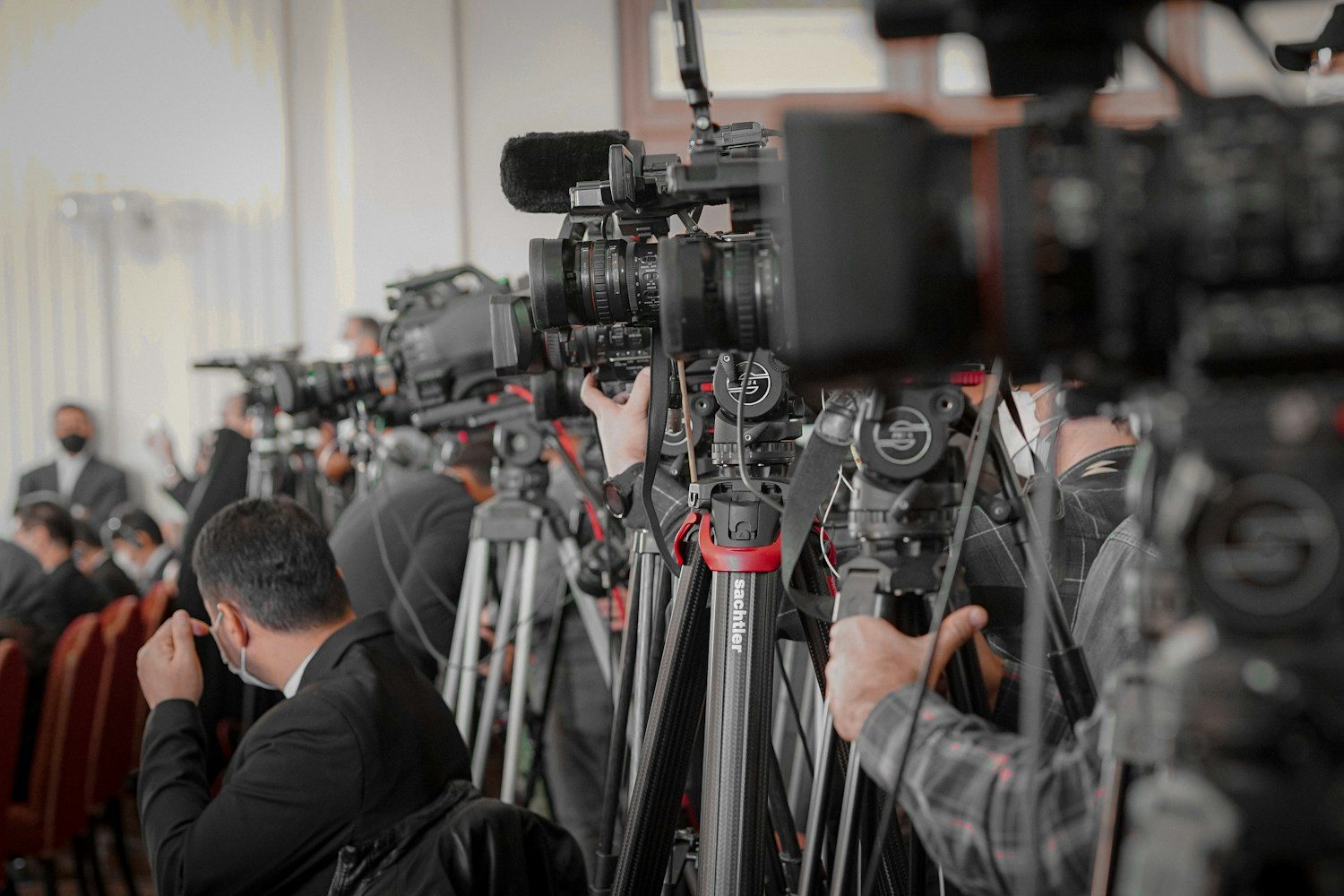 Basın toplantısında tripodlara dizilmiş televizyon kameraları ve gazeteciler